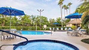 Una piscina con hidromasaje, sillas de descanso y sombrillas.