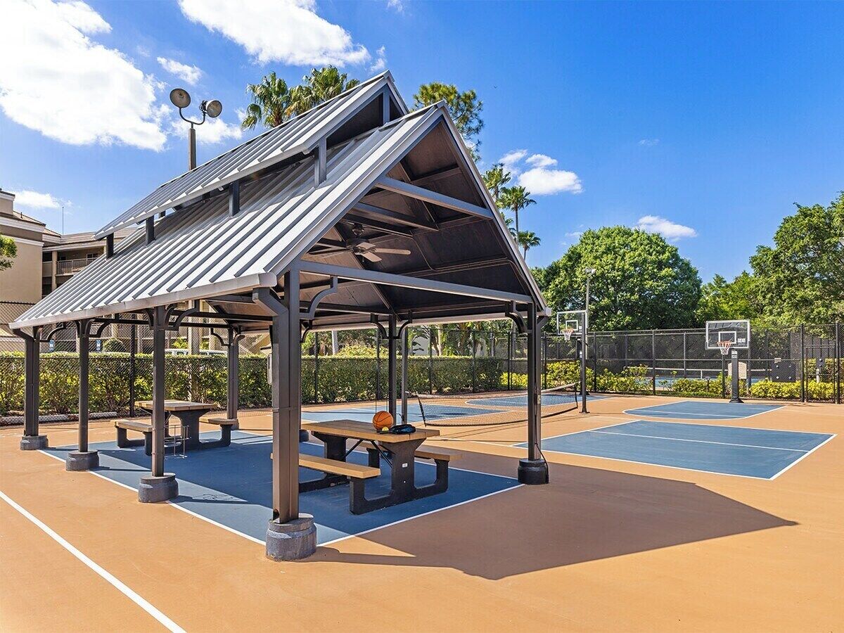 An outdoor basketball court with a covered pavilion, picnic tables, and a basketball hoop.