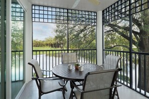 A covered patio with a round table and four chairs, a small potted plant, and a view of a green landscape through a metal grid. - 3 Bedroom Villa at Marriott Imperial Palms Resort (, Orlando)
