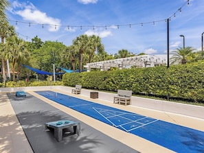 A sunny outdoor area with a shuffleboard court, seating, and a building in the background. - 3 Bedroom Villa at Marriott Imperial Palms Resort (, Orlando)