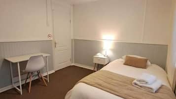 Ein Hotelzimmer mit Bett, Schreibtisch, Stuhl, Nachttisch und Wandleuchte.