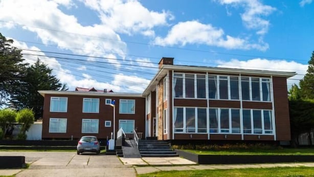 Un edificio de dos pisos con techo plano, ventanas amplias y una entrada visible con escalones.