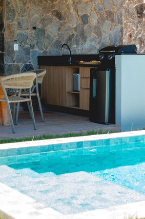 Ein Küchenbereich am Pool mit Steinwänden, einer Spüle, einem Kühlschrank und zwei Stühlen.