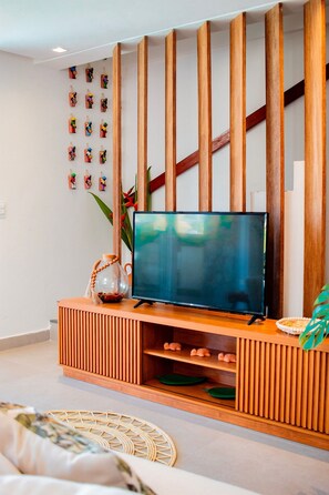 Ein modernes Wohnzimmer mit einem Flachbildfernseher auf einem Holzboden, einer Wand mit kleinen Figuren und einer Pflanze.