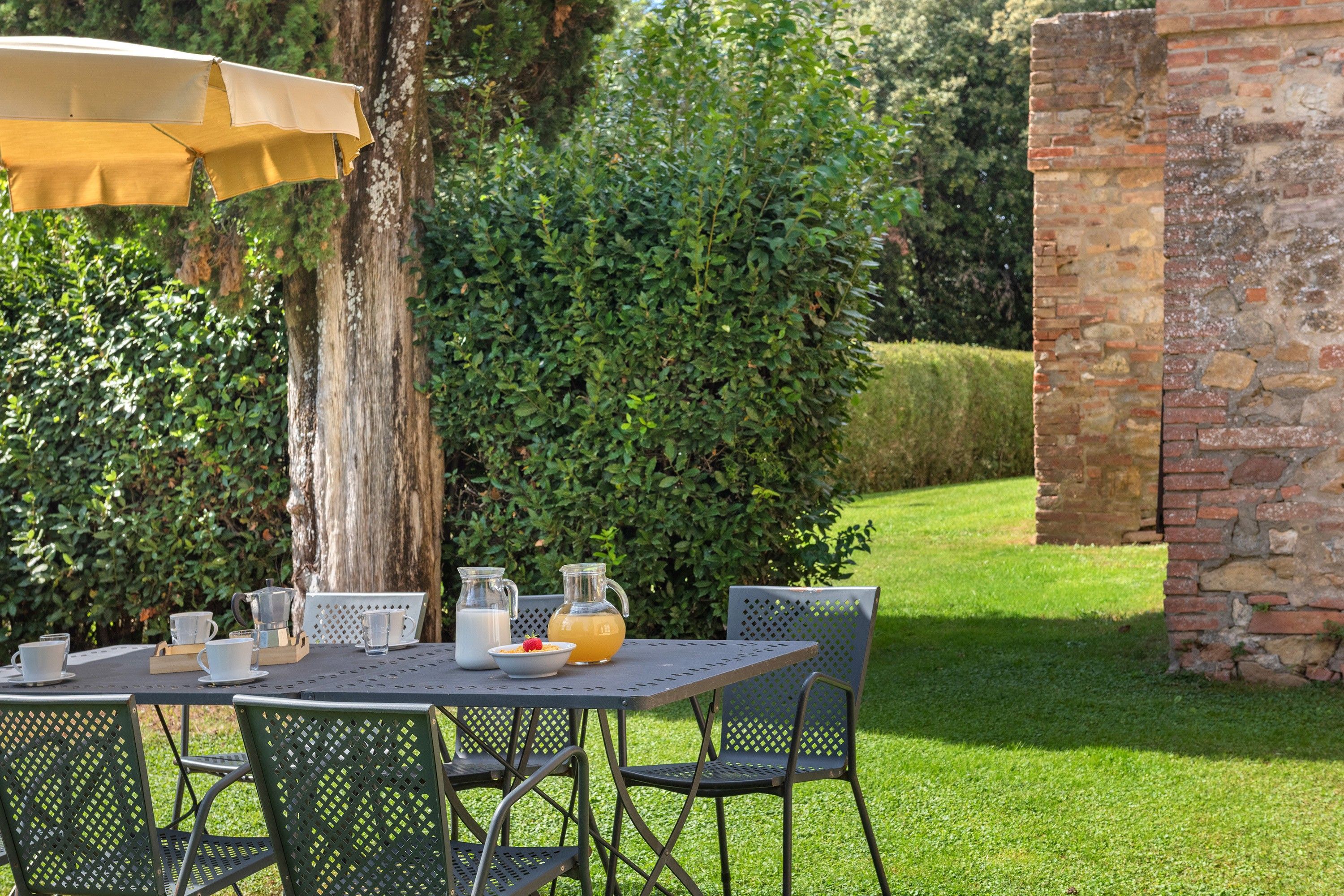 An outdoor dining area with a table set for two, a pitcher of water, a glass of milk, and a bowl of cereal with a strawberry.