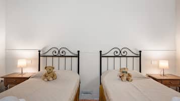 A room with two beds, each with a headboard, a bedside lamp, and a teddy bear on the bed.