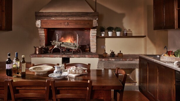 Una cucina con camino in mattoni, mobili in legno, un tavolo da pranzo con sedie e diversi oggetti da cucina.