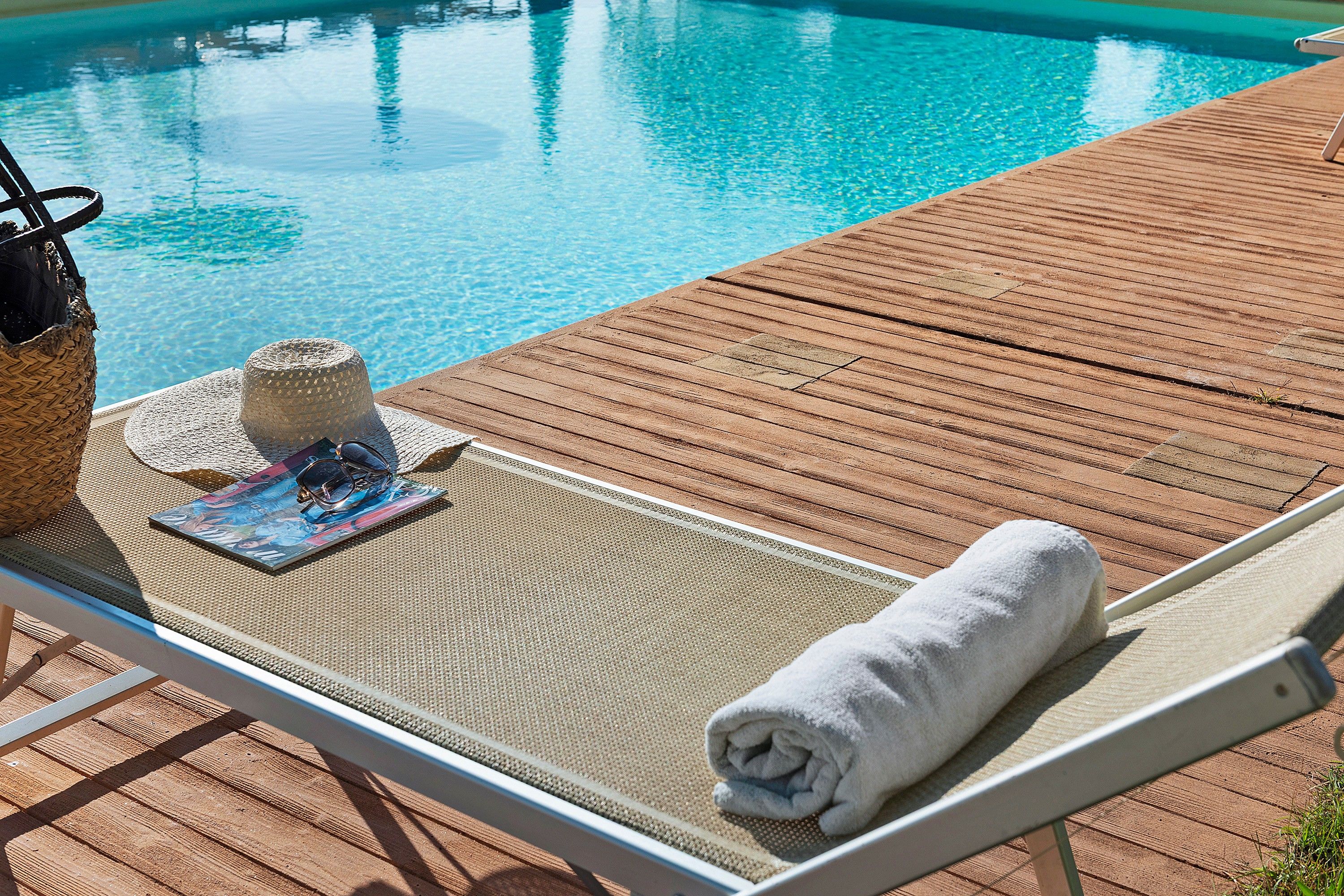 A poolside lounge chair with a towel, a magazine, and a hat.