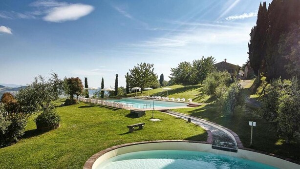 Ein Schwimmbecken mit einer umlaufenden Terrasse, einer Brücke und Blick auf die Landschaft.