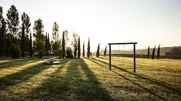 Eine grüne Wiese mit Schaukel und Tor, umgeben von Bäumen.