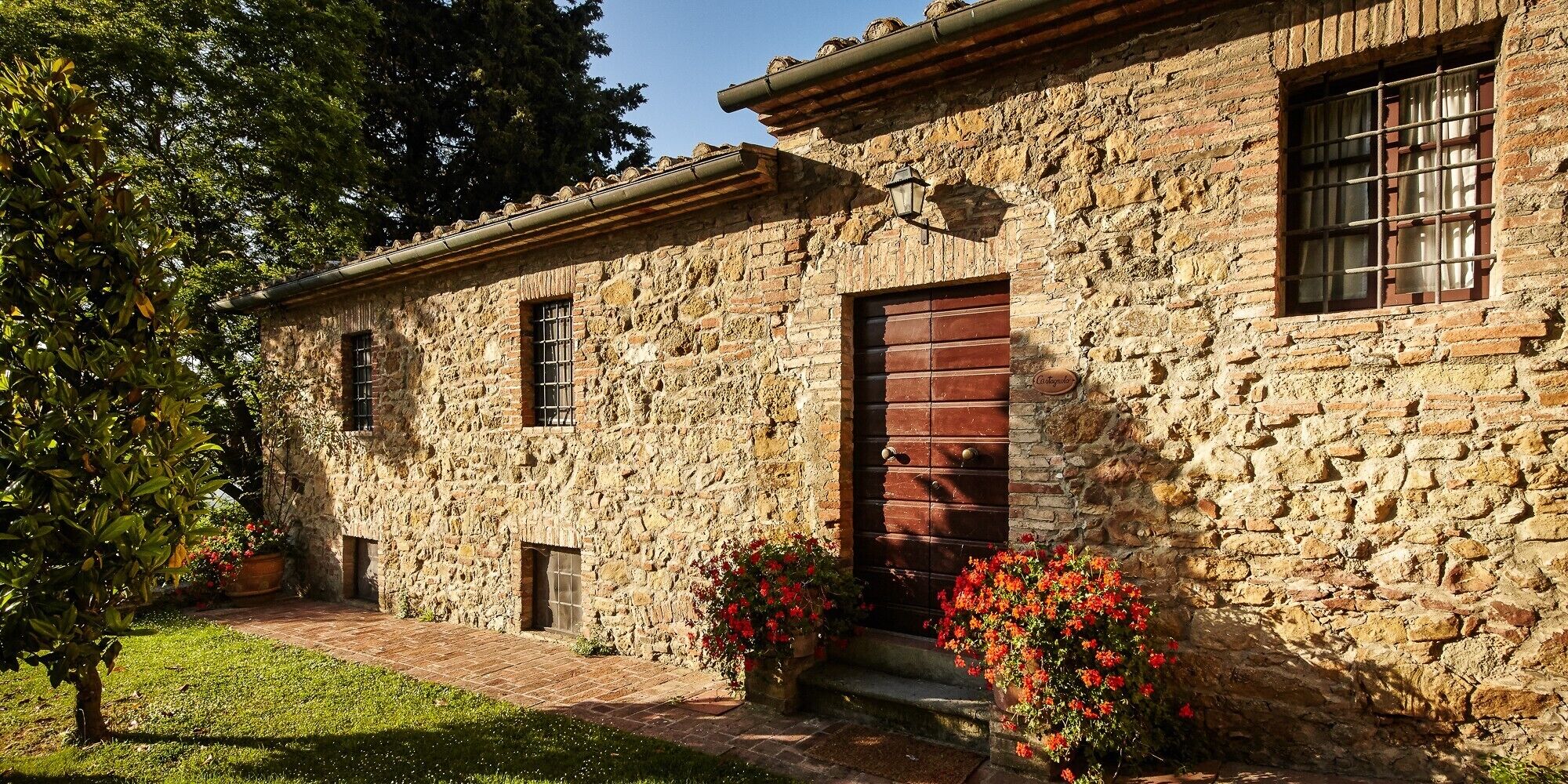 Un edificio in pietra con una porta e delle finestre in legno, immerso nel verde e circondato da fiori.