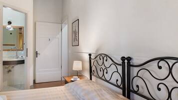 A bedroom with a bed, a bedside table with a lamp, a bathroom with a mirror, and a door.