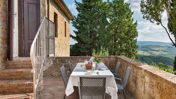Mesa para dos en una terraza con pared de piedra y vista al campo.