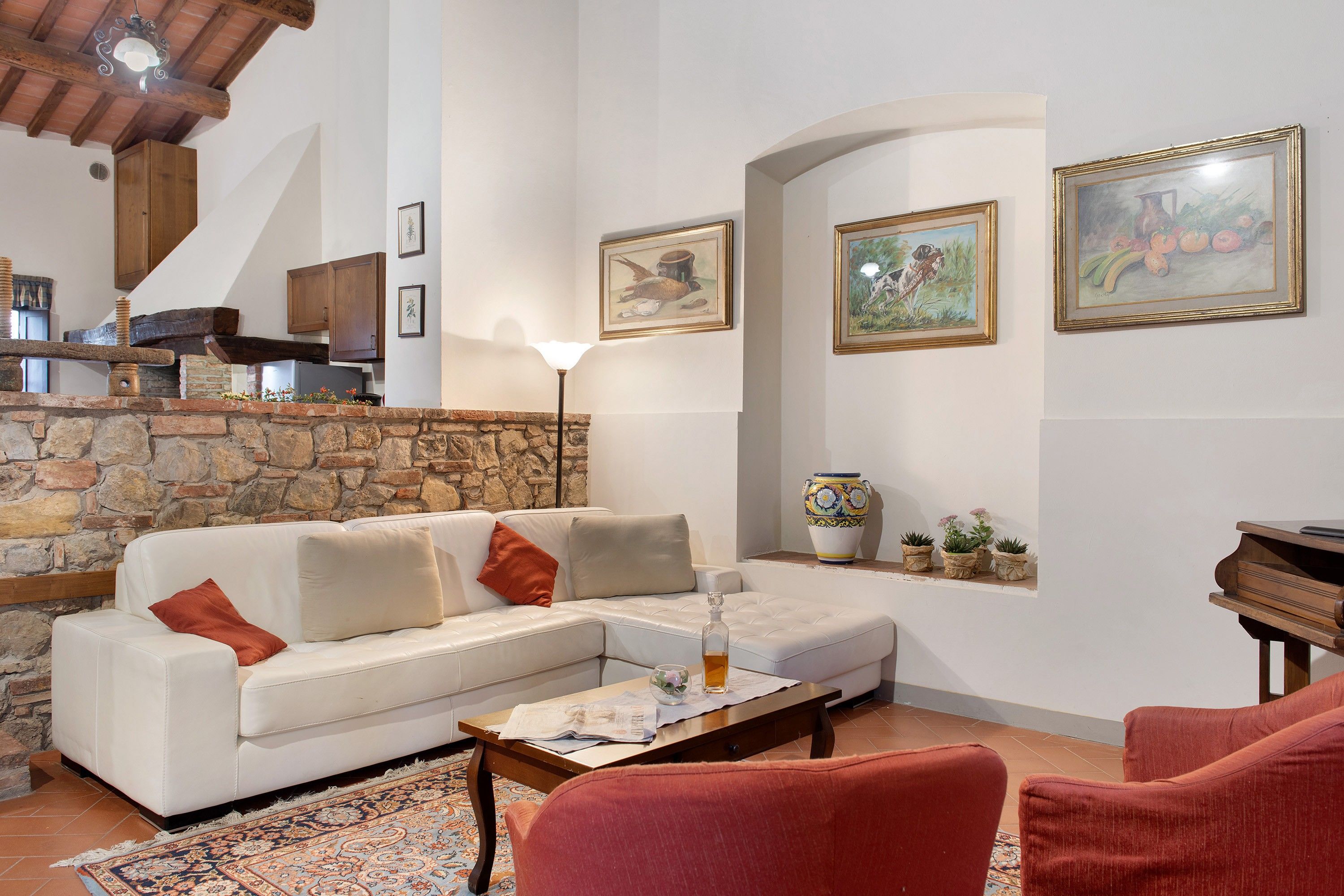 A living room with a white sofa, a red armchair, a coffee table with a newspaper, a stone fireplace, and a painting on the wall.