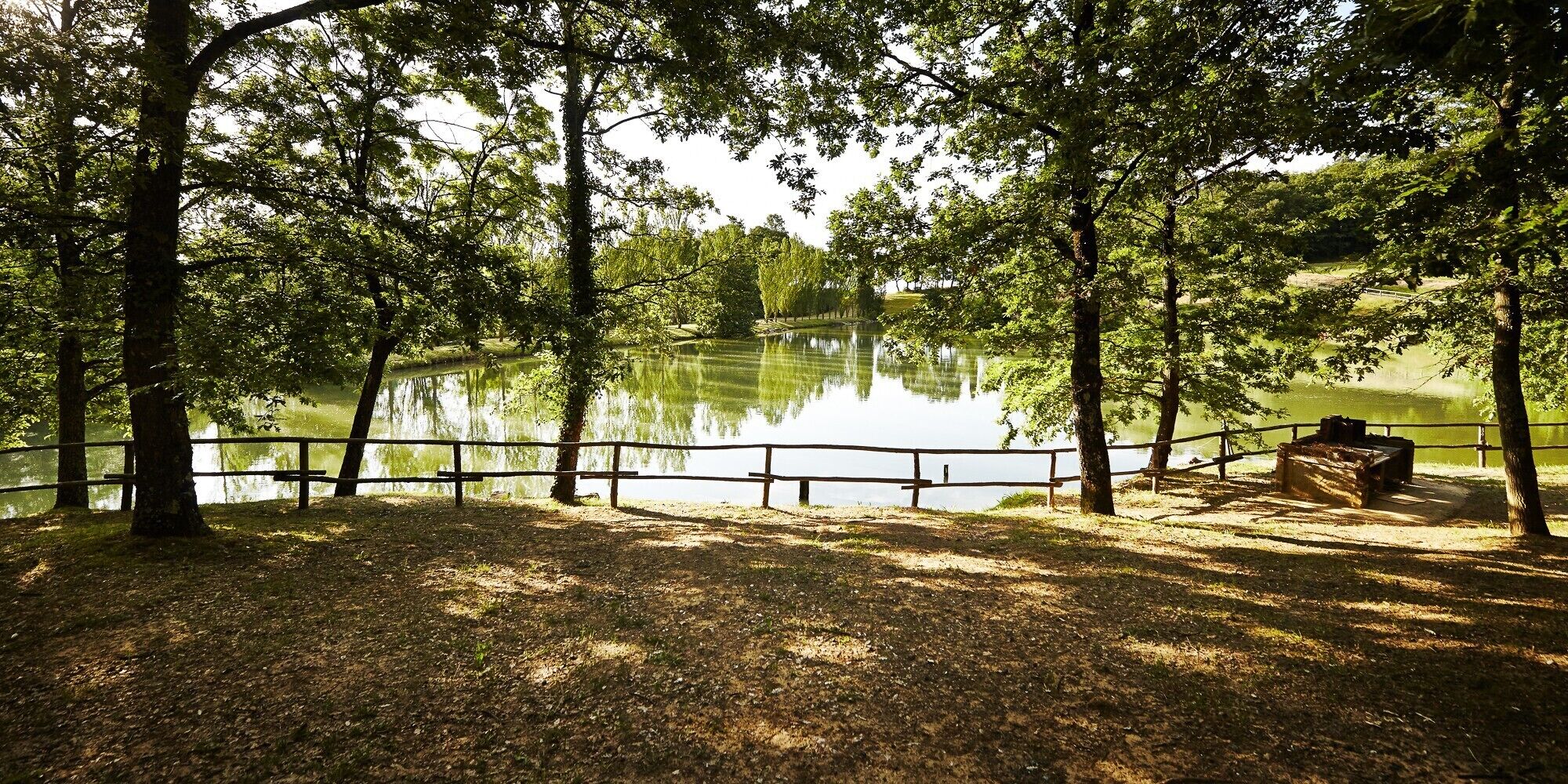 Un parc paisible au bord du lac, avec une clôture en bois, des arbres et des tables de pique-nique.