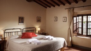 Ein Hotelzimmer mit einem Bett, zwei Nachttischen mit Lampen, einem Fenster mit Vorhängen und Wandbildern.