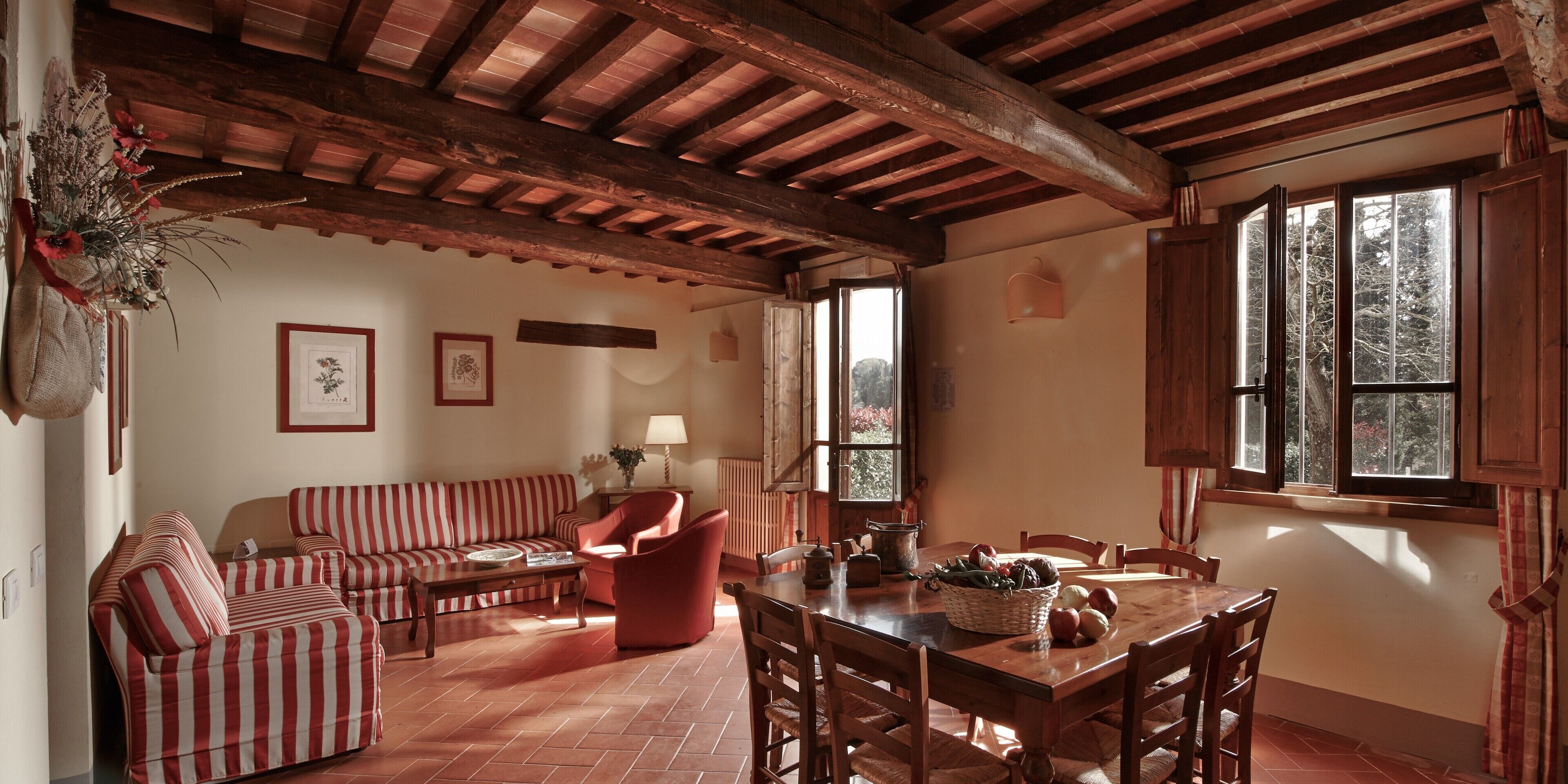 Ein rustikales Interieur mit Holzbalkendecke, einem Esstisch mit Stühlen, einer Couch und einem roten Sessel.