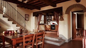 Ein Essbereich mit Holztisch und -stühlen, eine Treppe, eine Küche mit Holzschränken und ein gestreiftes Sofa.