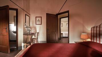 Une chambre d’hôtel avec un lit, un bureau et une chaise, une lampe, et une salle de bain visible à travers une porte ouverte.