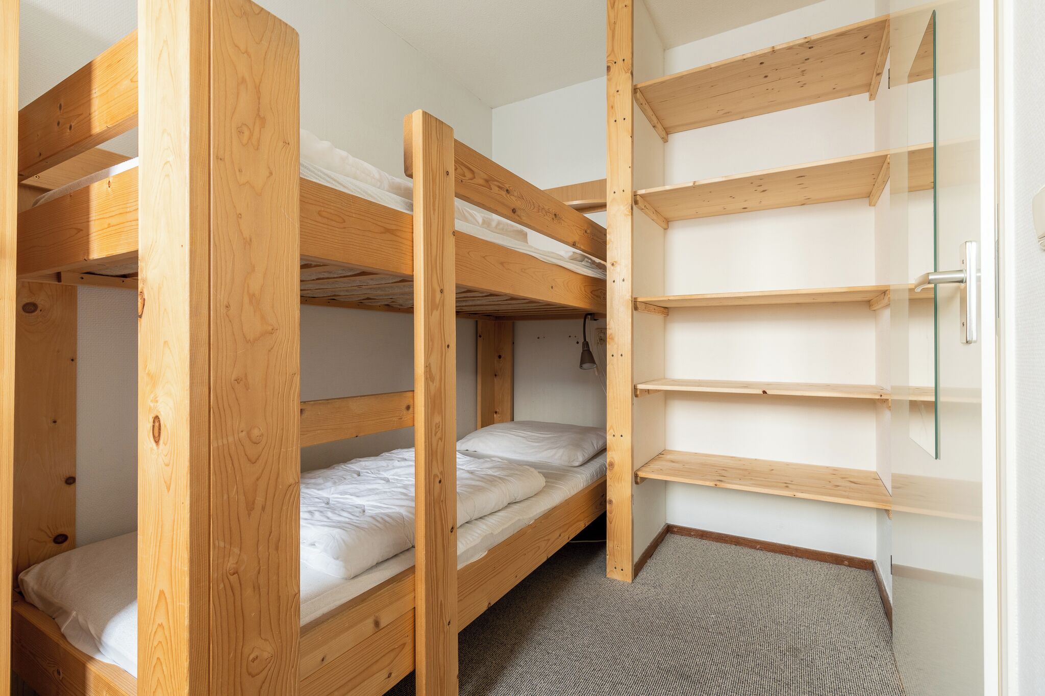 Een slaapkamer met stapelbedden, houten frames, een klein bureau en een glazen deur.