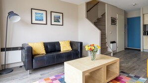 A modern living room with a black leather sofa, a wooden coffee table, and a colorful rug. - Comfortable vacation apartment on Ameland with access to a pool; dogs welcome (Hollum)