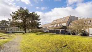 A modern building with multiple windows and a sloped roof. - Comfortable vacation apartment on Ameland with access to a pool; dogs welcome (Hollum)