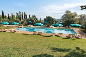 A rectangular swimming pool with a surrounding deck, equipped with multiple lounge chairs and umbrellas.