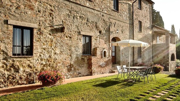 Ein Steinhaus mit einer Terrasse, die Sitzgelegenheiten und einen weißen Sonnenschirm bietet.
