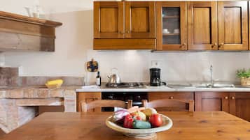 Una cocina con gabinetes de madera, salpicadero de ladrillo, una estufa a gas y un tazón de verduras sobre la mesa.