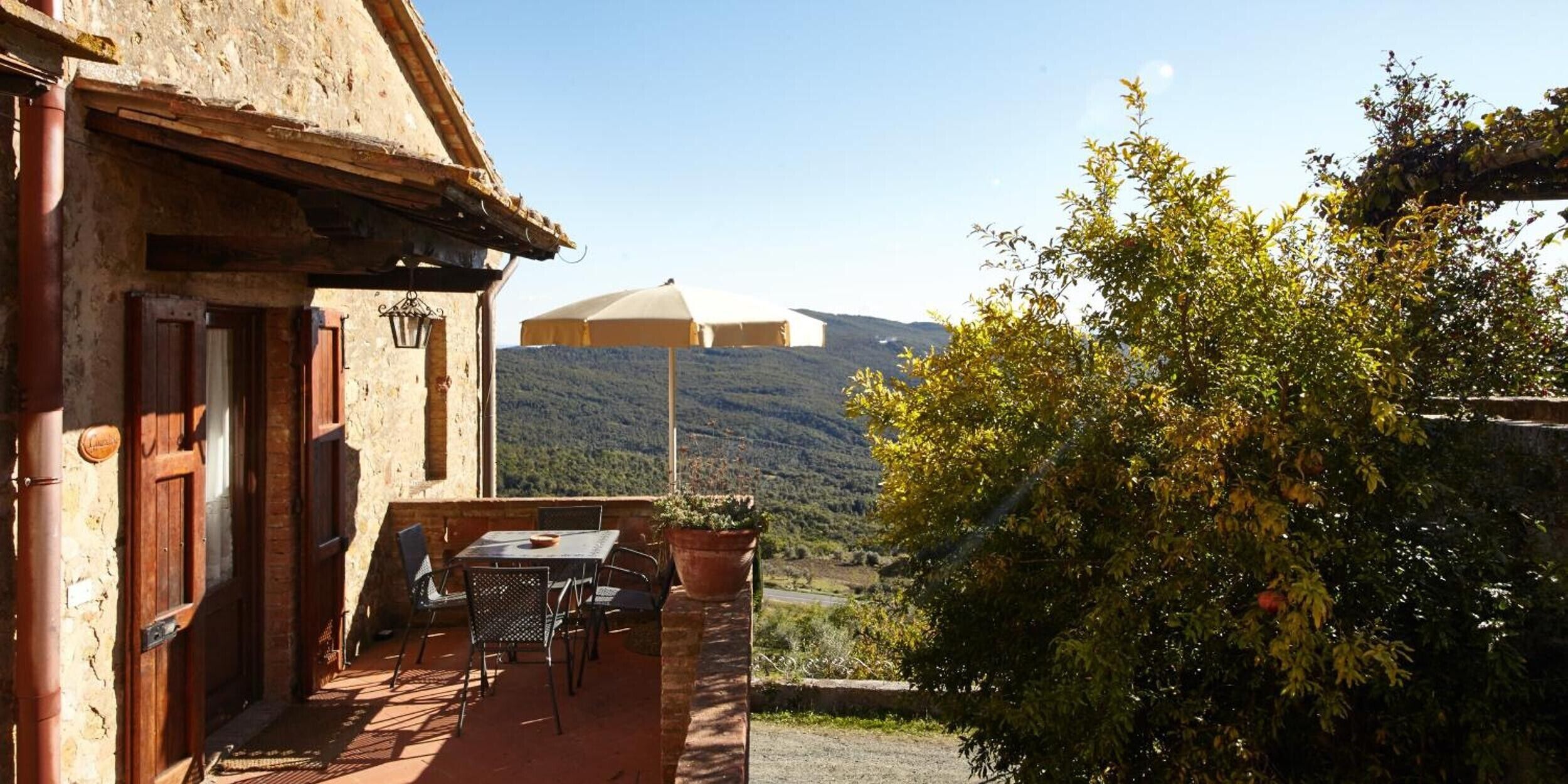 Un espace extérieur aménagé dans un style rustique, avec une table et des chaises, une porte en bois et une vue sur une chaîne de montagnes.