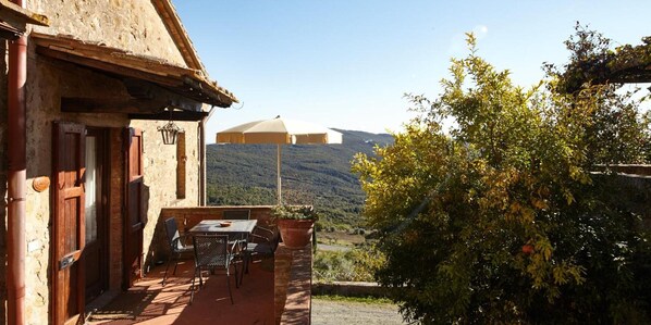 A rustic outdoor seating area with a table and chairs, a wooden door, and a view of a mountain range.
