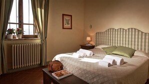 Ein Hotelzimmer mit einem Bett, einem Nachttisch, einer Lampe, einem Heizkörper, einem Fenster mit Vorhängen und einer Zeitschrift auf einem Tisch.