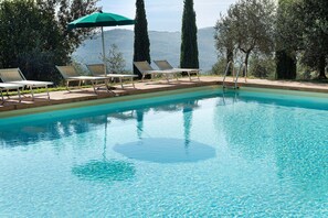 A clear swimming pool with lounge chairs and a green umbrella.