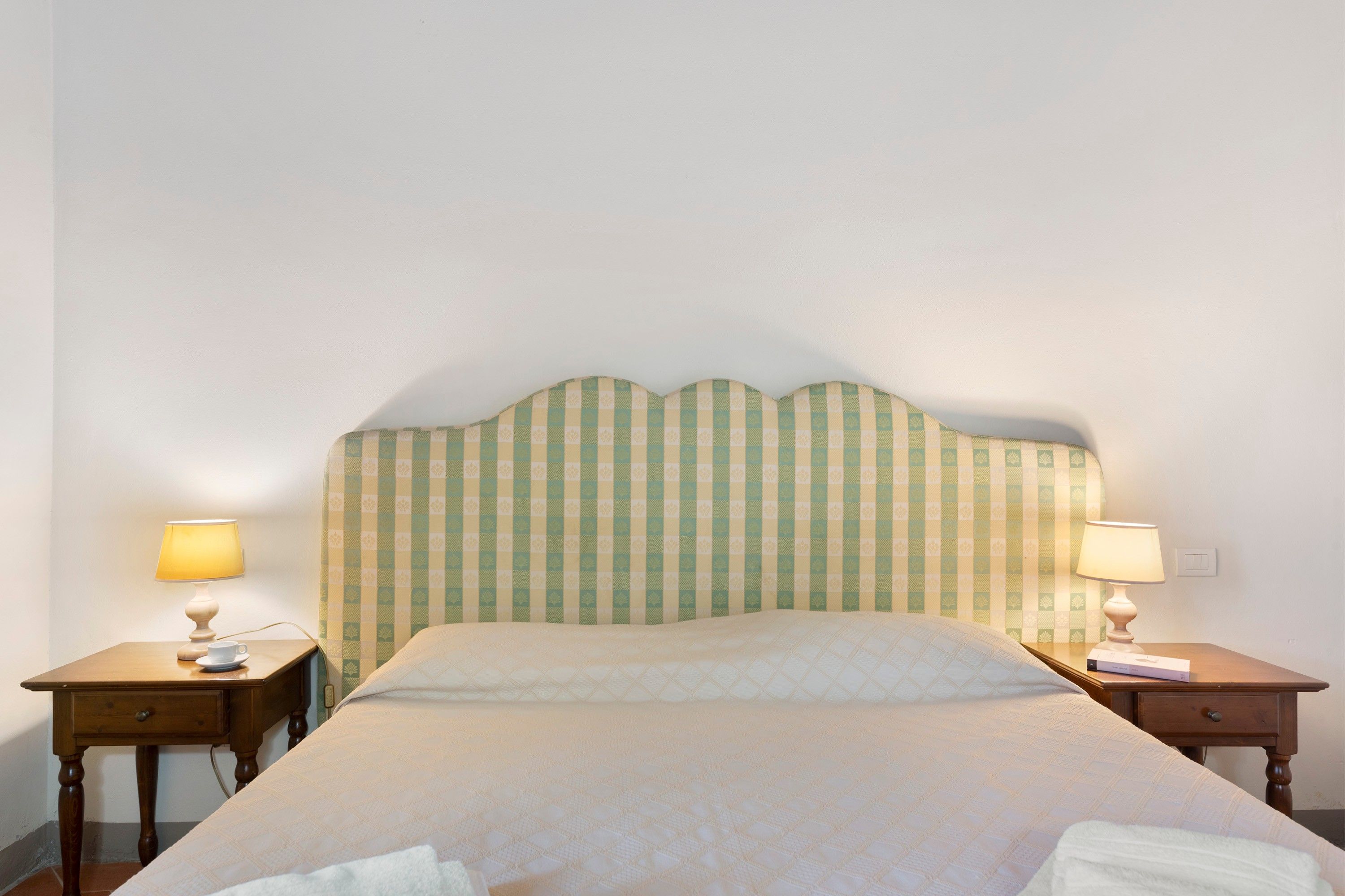 Habitación de hotel con una cama individual, dos mesitas de noche y un cabecero con estampado de cuadros.