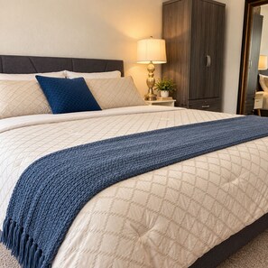 Un lit bien fait, avec une couette matelassée, un plaid bleu et une lampe de chevet.