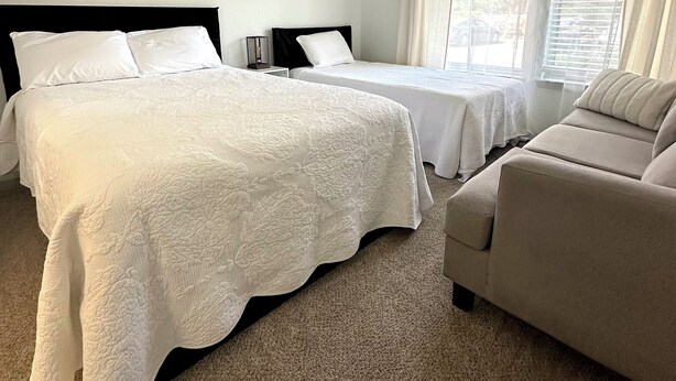 Une chambre d’hôtel avec deux lits, un canapé et une grande fenêtre avec des rideaux.