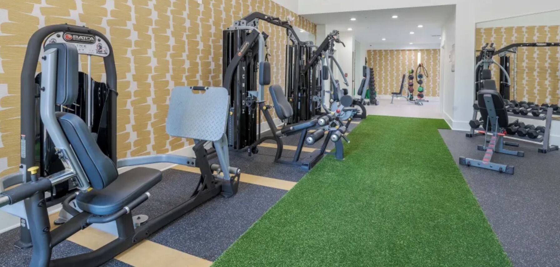 A gym with various exercise equipment, a green artificial turf, and a patterned wall.