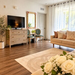 Un salon comprenant un téléviseur, un canapé, deux fauteuils, une table basse, un miroir et une plante en pot.