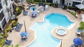 Une piscine entourée d’un espace aménagé avec des palmiers, comprenant des chaises longues et des parasols.