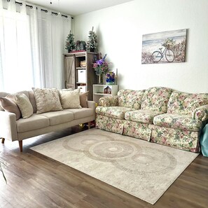 Un salon avec un canapé beige, un canapé à motifs floraux, un meuble en bois et un tableau représentant un vélo.