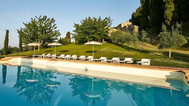 Une piscine entourée d’arbres et d’une colline, avec des chaises longues et des parasols.