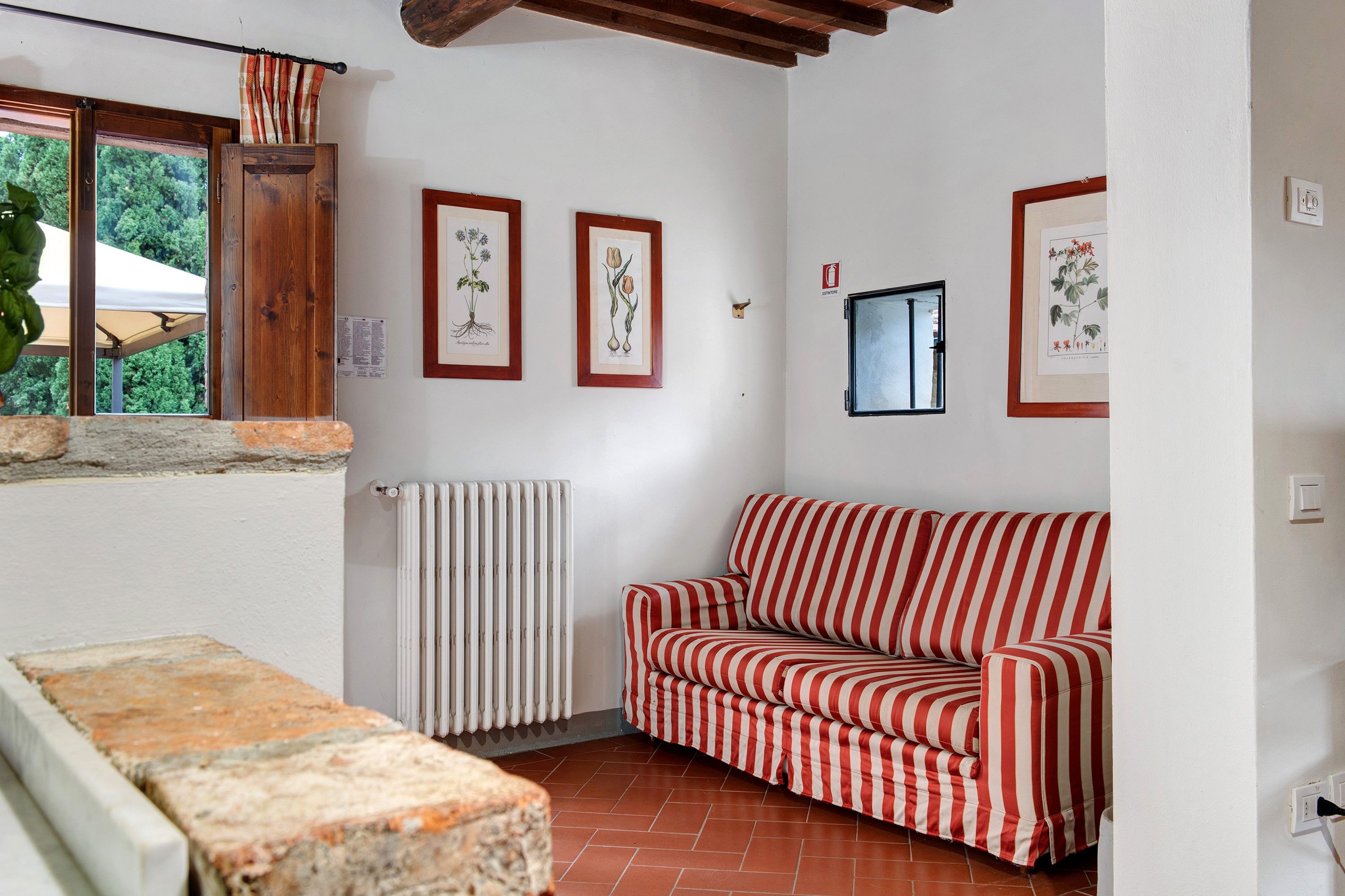 Una habitación con un sofá a rayas rojas y blancas, un radiador e ilustraciones botánicas enmarcadas en la pared.