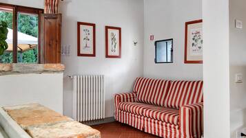 Una habitación con un sofá a rayas rojas y blancas, un radiador e ilustraciones botánicas enmarcadas en la pared.