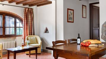 Un comedor con una mesa de madera, sillas, un florero con flores, una botella de vino y una hogaza de pan.
