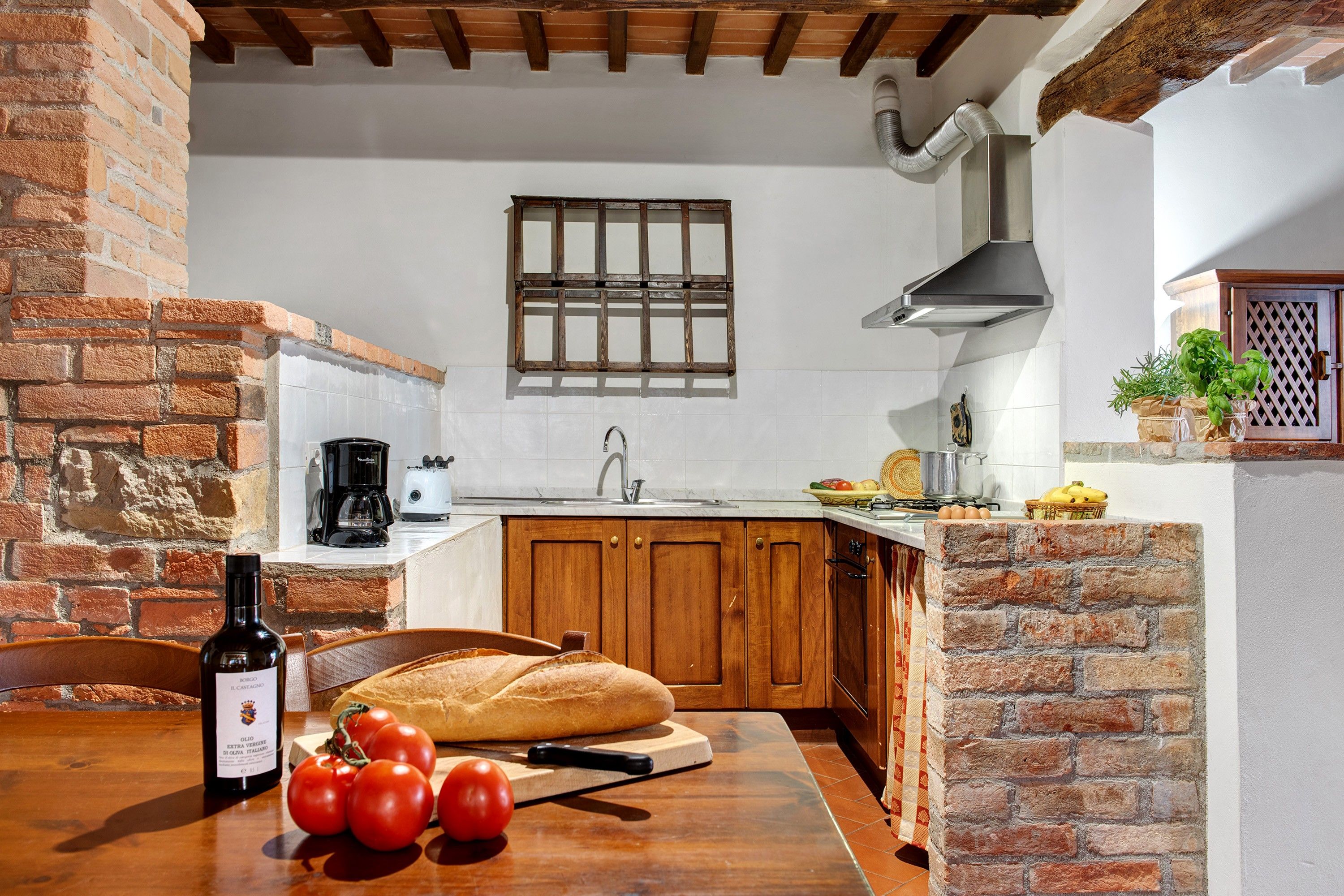 A kitchen with a brick wall, wooden cabinets, a window, and a hanging pot rack.