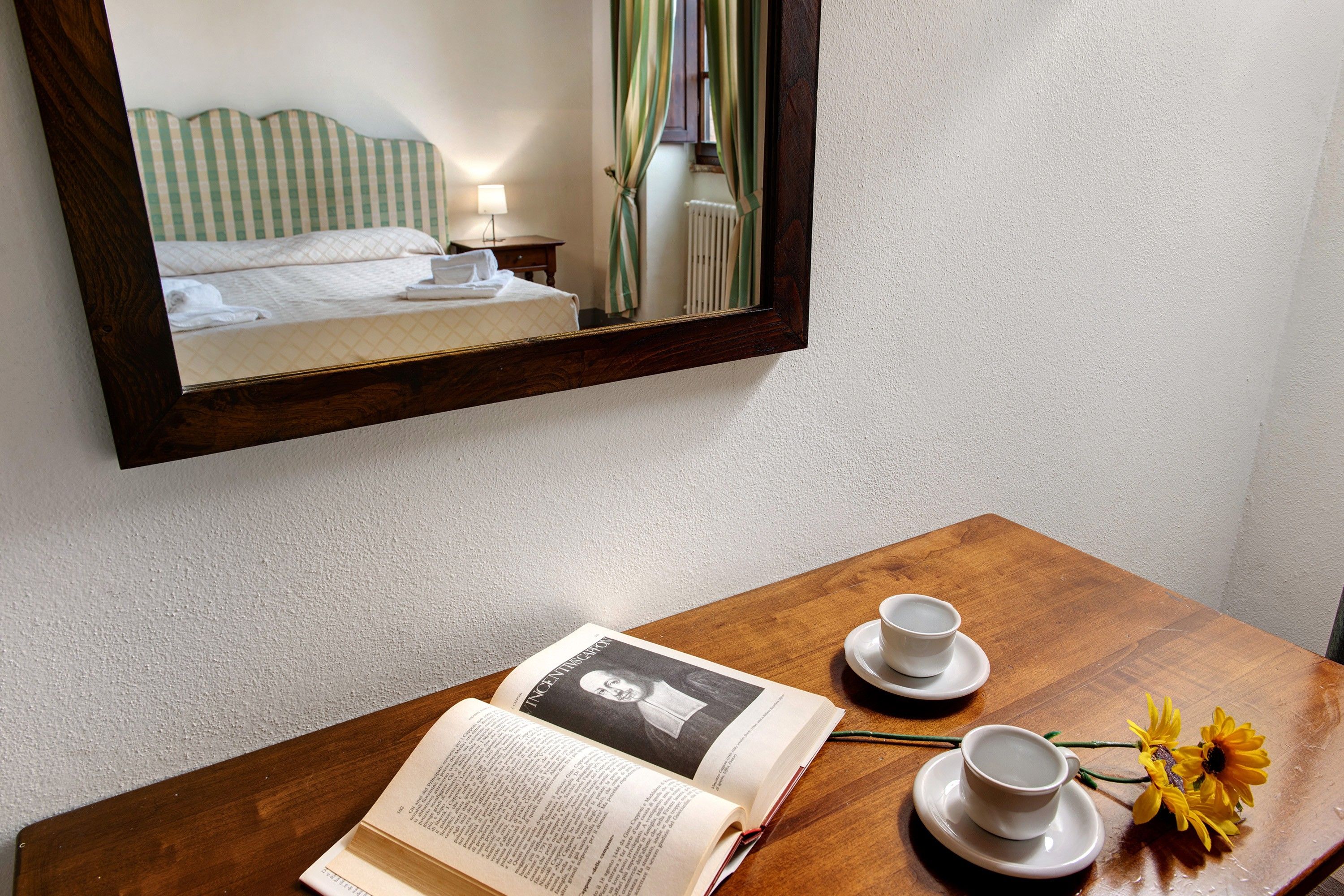 Ein Hotelzimmer mit einem Holztisch, einem Buch, einer Tasse, einem Untertasse und einer Vase mit Blumen.