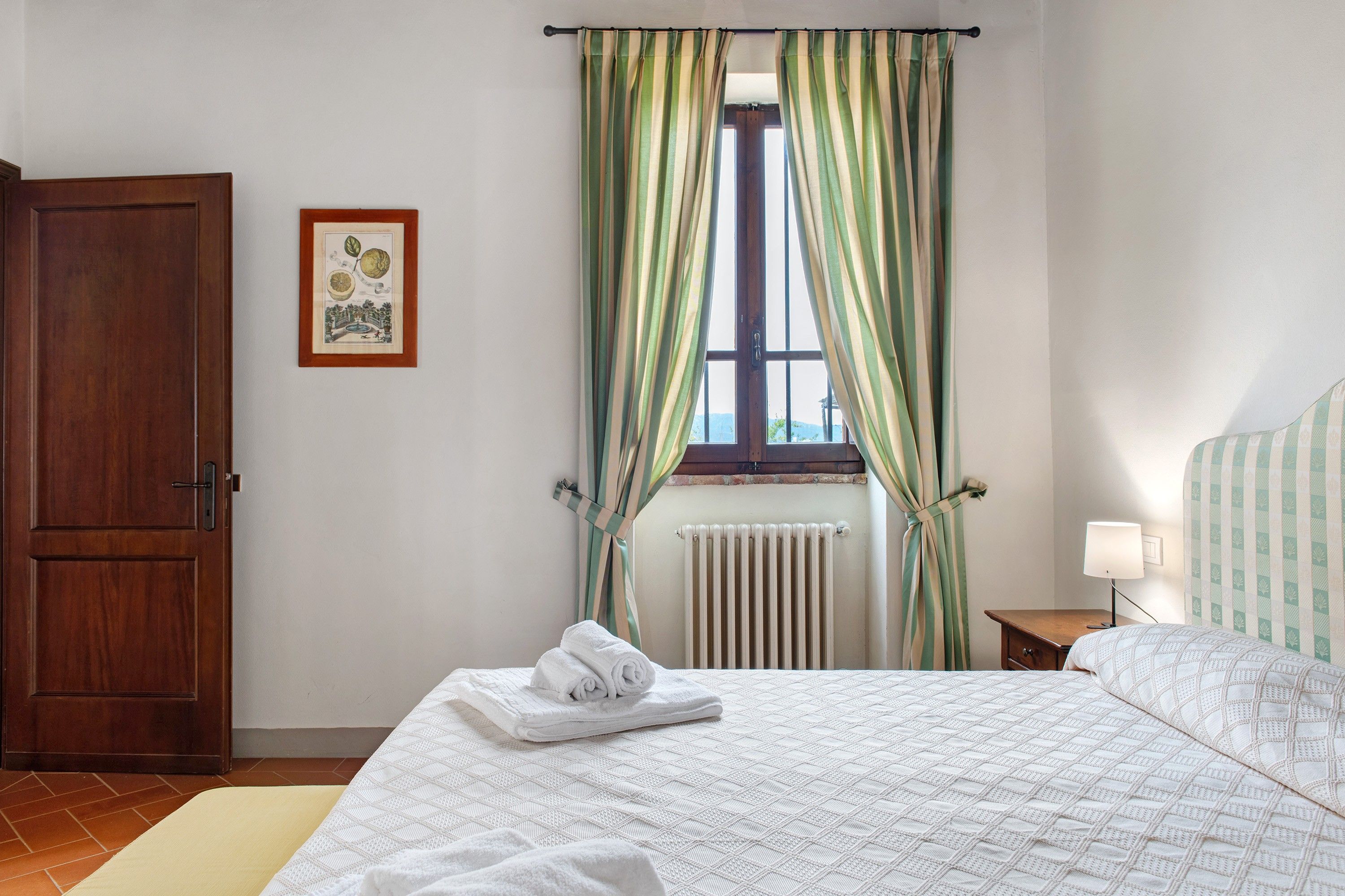 A bedroom with a bed, a radiator, a door, and a framed picture on the wall.