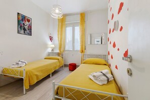 A room with two beds, a window with yellow curtains, a painting on the wall, and a clock. - Apartment 'Guest House Nuvola' with Shared Garden, Wi-Fi and Air Conditioning (Lucino)