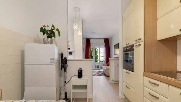 Et kompakt køkken med et køleskab, kaffemaskine og et lille bord med kop og bestik.