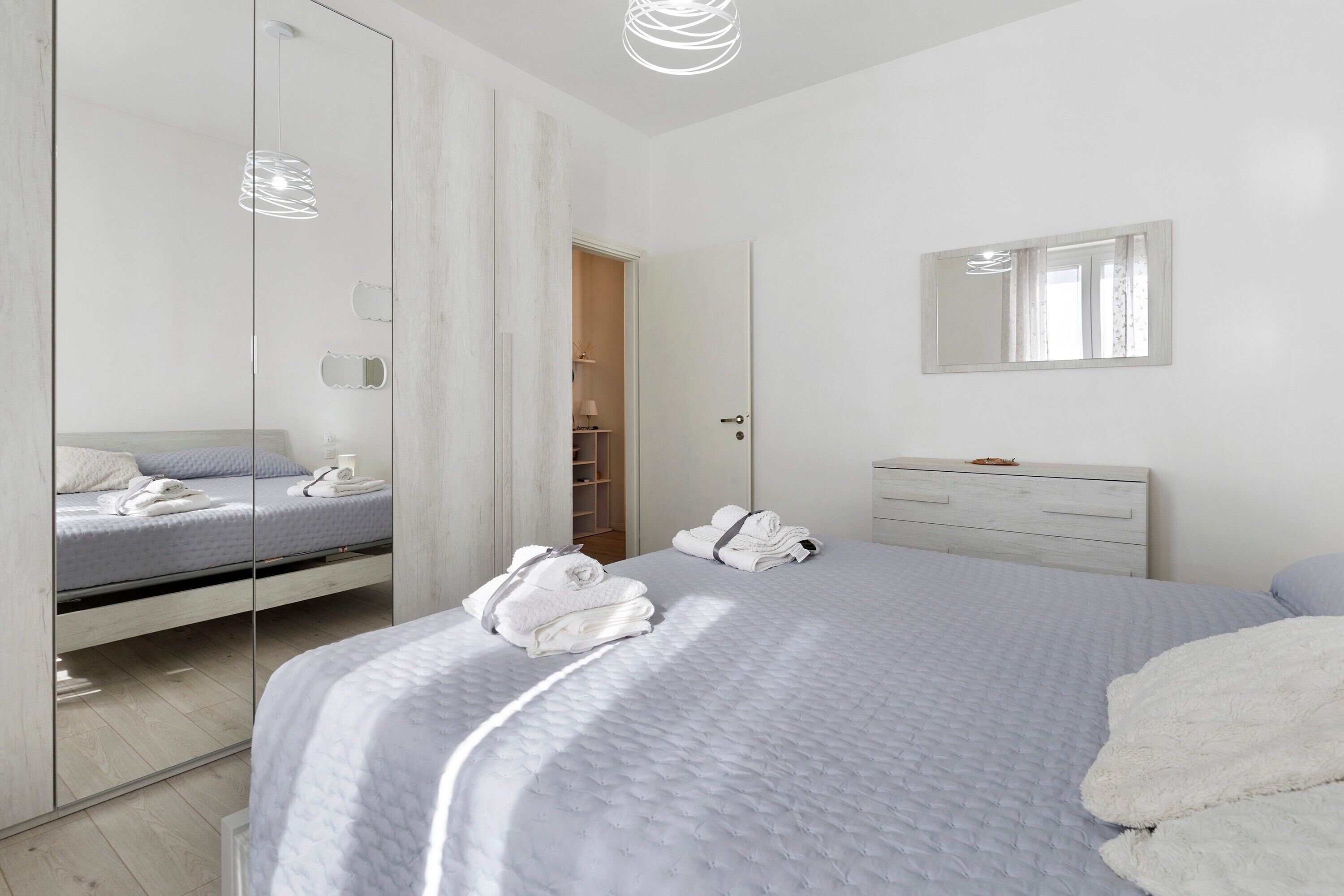A modern bedroom with a bed, a dresser, a mirror, and a walk-in closet.